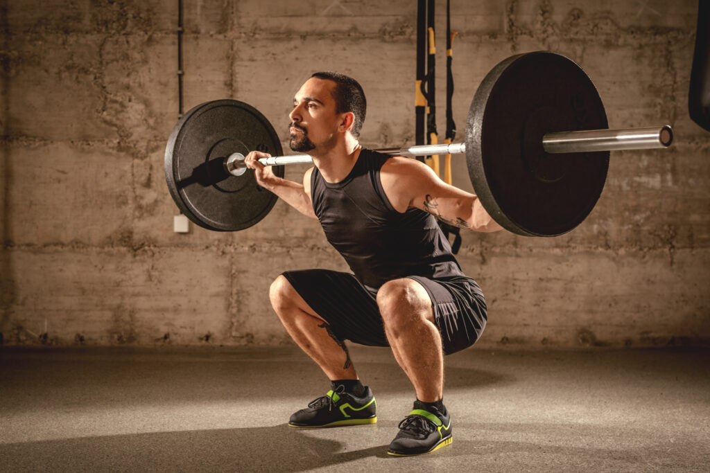 handsome young muscular man doing squat exercise with barbell gym